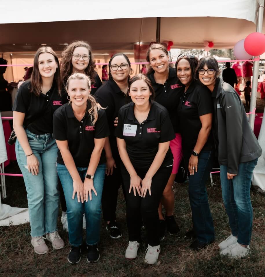 Group of NBCF team members standing together at a breast cancer awareness event tent.
